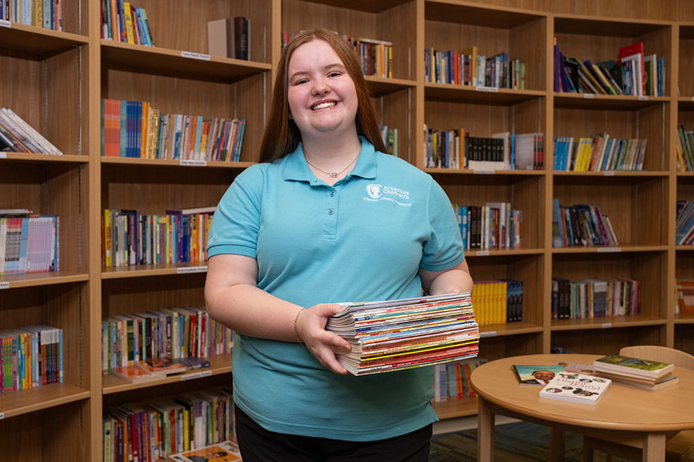Photo of Arkansas Children's volunteer holding books in library.